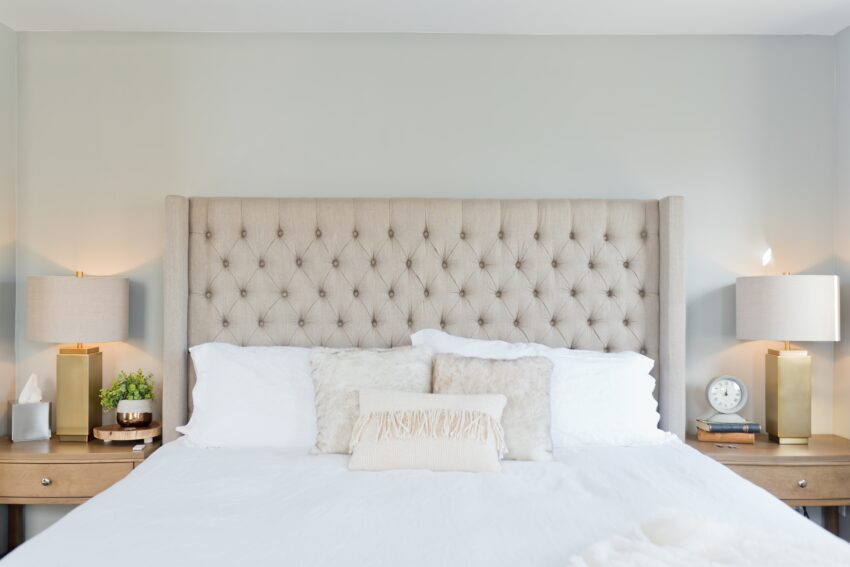 A bedroom with bed, curtains, and pillows in soft beige, gray and metallic tones.