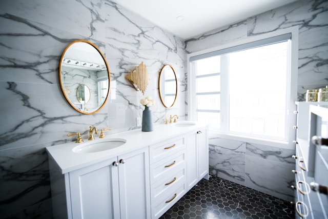 Decorative elements like framed mirrors can add a nice touch of nostalgic charm. Alt text: Bathroom with white tiles, cupboards, golden faucets and framed mirrors